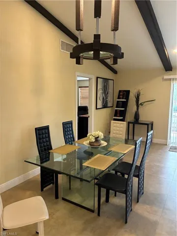Dining area featuring a prominent chandelier and vaulted ceiling with dark wood beams