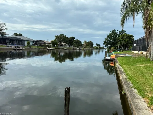 Waterfront canal property featuring a concrete seawall, wooden dock, lush green lawn, and mature palm trees