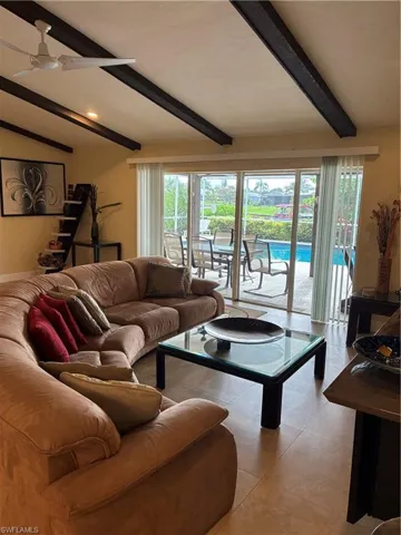 Vaulted ceiling with exposed wood beams, large format floor tiles, and sliding glass doors opening to an outdoor patio with a swimming pool