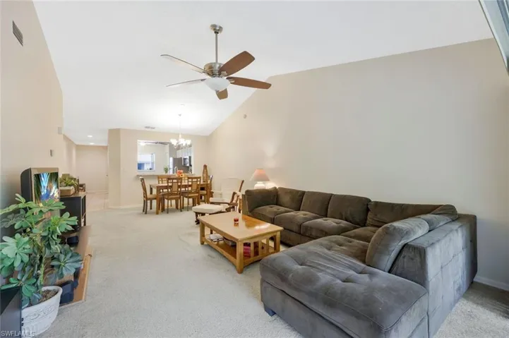 Carpeted living room with high vaulted ceiling and ceiling fan with notable chandelier