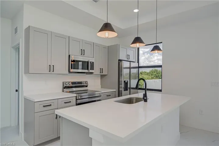 Kitchen featuring light marble finish floors, stainless steel appliances, gray cabinetry, an island with sink, and light countertops