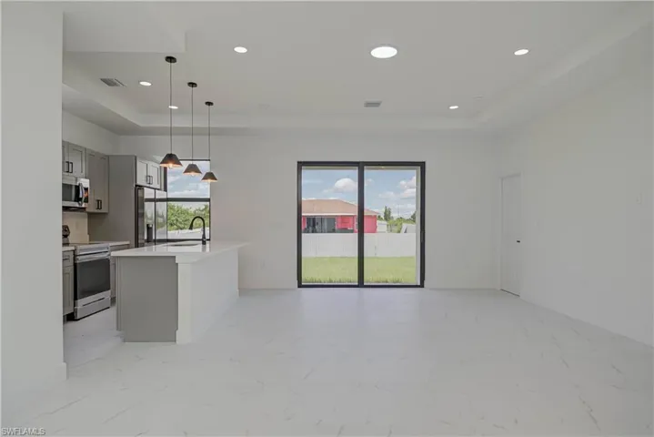 Kitchen with light marble finish flooring, a tray ceiling, appliances with stainless steel finishes, light countertops, and open floor plan