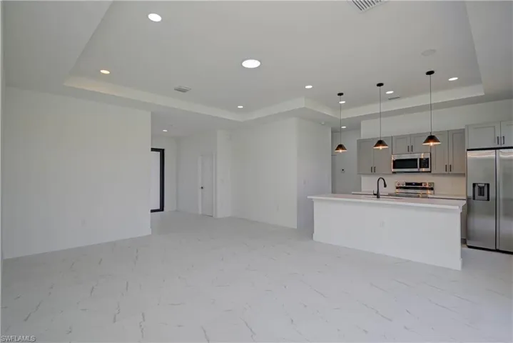 Kitchen with a raised ceiling, appliances with stainless steel finishes, light marble finish floors, open floor plan, and recessed lighting