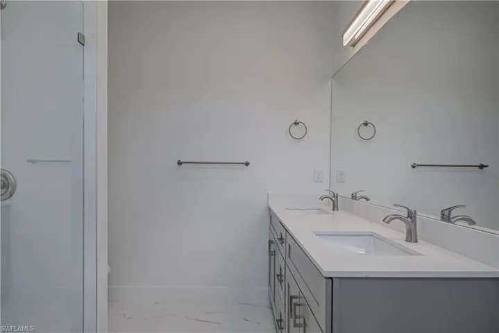 Full bath featuring marble finish floors, double vanity, and a shower