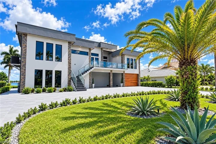Modern exterior with stacked stone accents, a glass-paneled balcony, a wood-finish garage door, and a manicured lawn