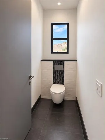 Recessed lighting illuminates the space, featuring dark tile flooring and a wall-mounted toilet