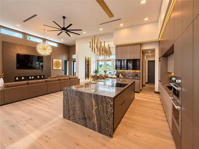 Open-concept living space featuring wood-finish flooring, a kitchen island with a waterfall countertop, integrated stainless steel appliances, and a built-in fireplace