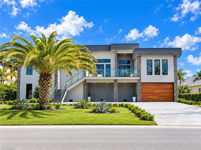 Modern architectural design featuring stacked stone accents, a wood-finish garage door, and a glass-paneled balcony