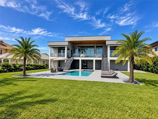 Contemporary architecture with a flat roofline, expansive windows, glass balcony railings, a ground-level swimming pool, and a spacious lawn area