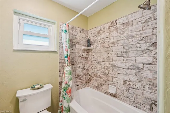 Full bath with shower / tub combo with curtain and a textured wall