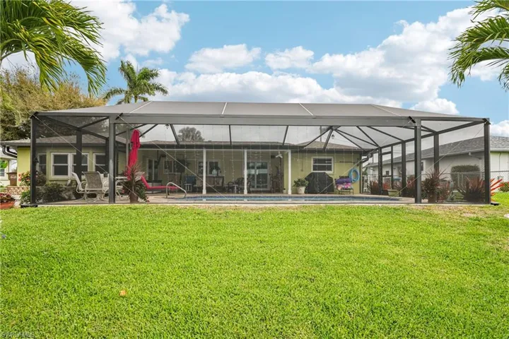 Back of property with glass enclosure, an outdoor pool, a lawn, and a patio