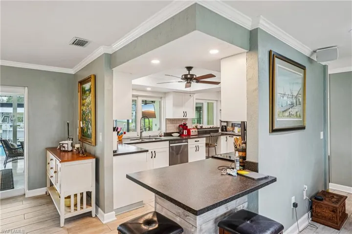 Kitchen with ornamental molding, a breakfast bar, a peninsula, white cabinets, and a ceiling fan