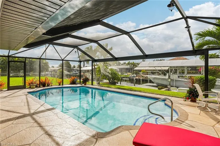 Swimming pool featuring a sunroom, boat lift, a dock, glass enclosure, and a patio