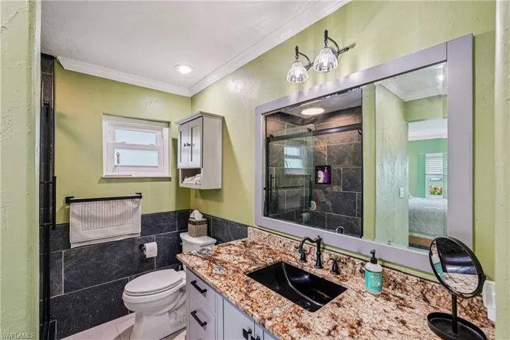Ensuite bathroom with vanity, ornamental molding, a stall shower, tile walls, and plenty of natural light