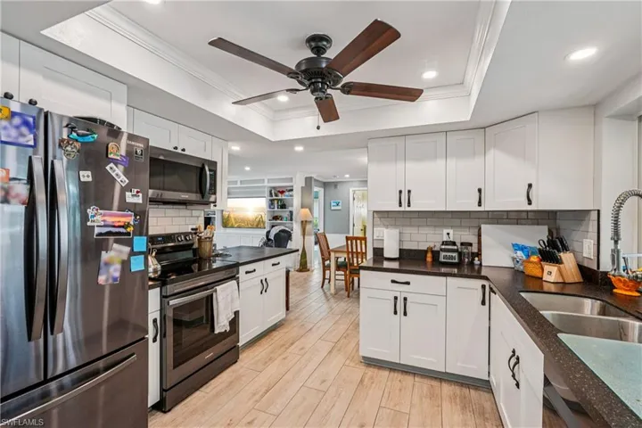 Kitchen with stainless steel appliances, crown molding, white cabinets, ceiling fan, and light wood-style floors