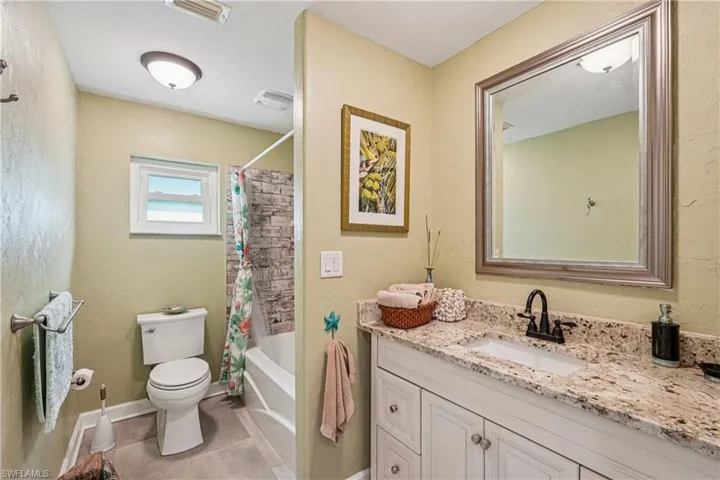 Bathroom featuring a textured wall, vanity, shower / tub combo with curtain, and light tile patterned floors