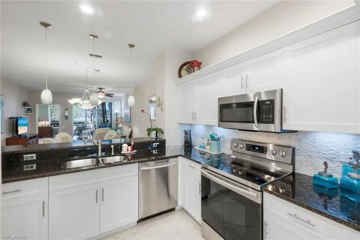 Kitchen with stainless steel appliances, open floor plan, white cabinets, dark stone counters, and decorative light fixtures