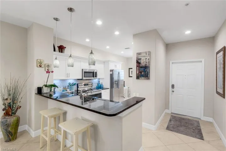Kitchen with a peninsula, stainless steel appliances, decorative light fixtures, a kitchen bar, and backsplash