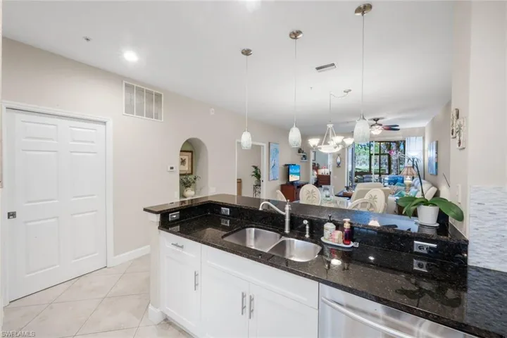 Kitchen with dark stone counters, white cabinetry, stainless steel dishwasher, hanging light fixtures, and ceiling fan