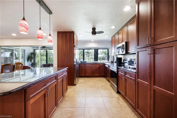 Kitchen featuring stainless steel appliances, ceiling fan, hanging light fixtures, recessed lighting, and dark stone countertops