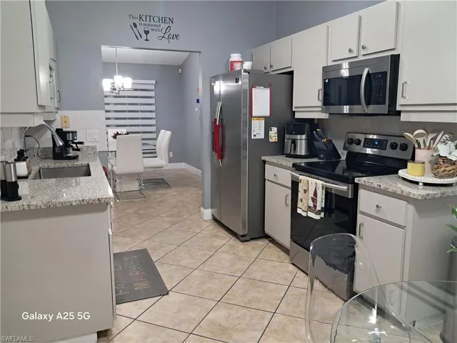Kitchen featuring stainless steel appliances, sink, light tile patterned floors, white cabinets, and pendant lighting