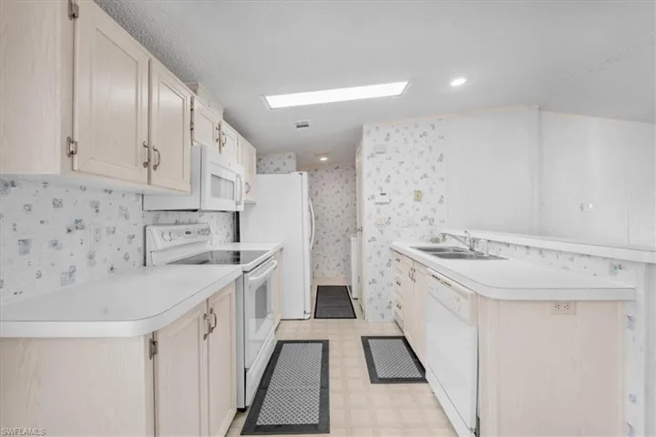 Kitchen with light floors, white appliances, a peninsula, light countertops, and light wood finish cabinets