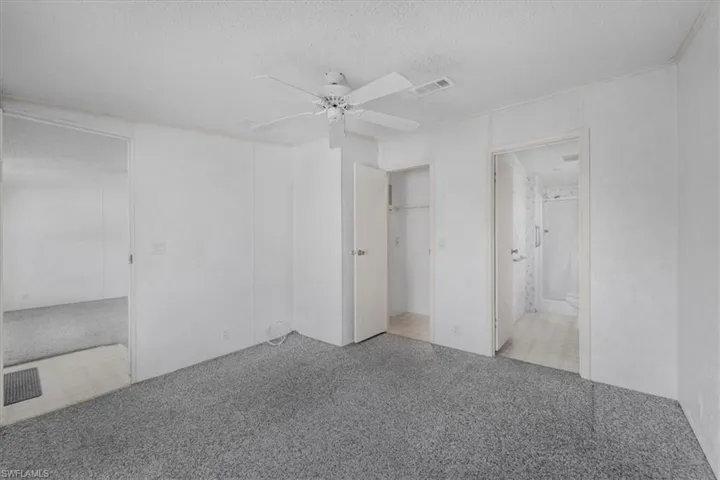 Unfurnished bedroom with a textured ceiling, a ceiling fan, a closet, light colored carpet, and ensuite bath