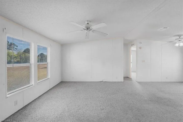 Spare room with ceiling fan, a textured ceiling, a decorative wall, and light carpet