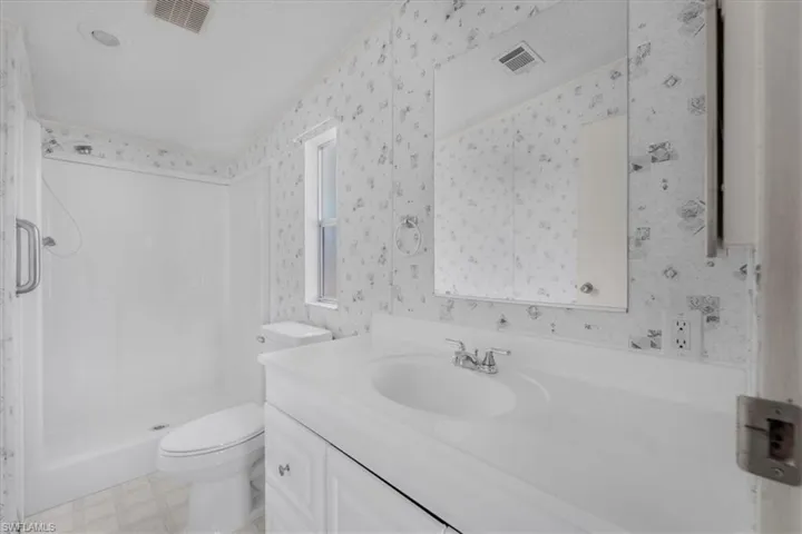 Full bathroom with vanity, light floors, a shower stall, and wallpapered walls