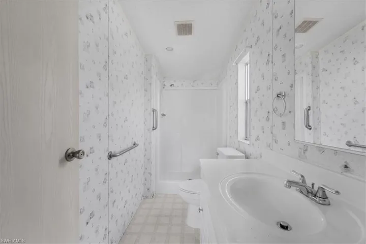 Bathroom featuring vanity, a stall shower, light floors, and wallpapered walls