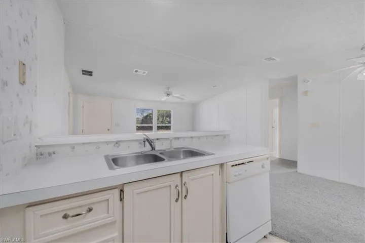 Kitchen featuring ceiling fan, dishwasher, light countertops, and light colored carpet