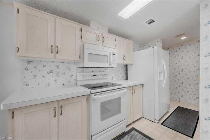 Kitchen with white appliances, light flooring, light countertops, wallpapered walls, and recessed lighting
