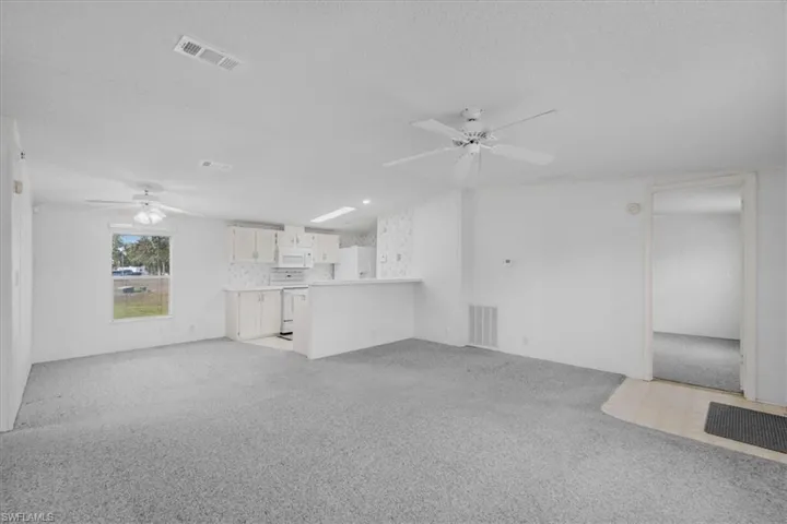 Unfurnished living room featuring ceiling fan, light carpet, and a textured ceiling