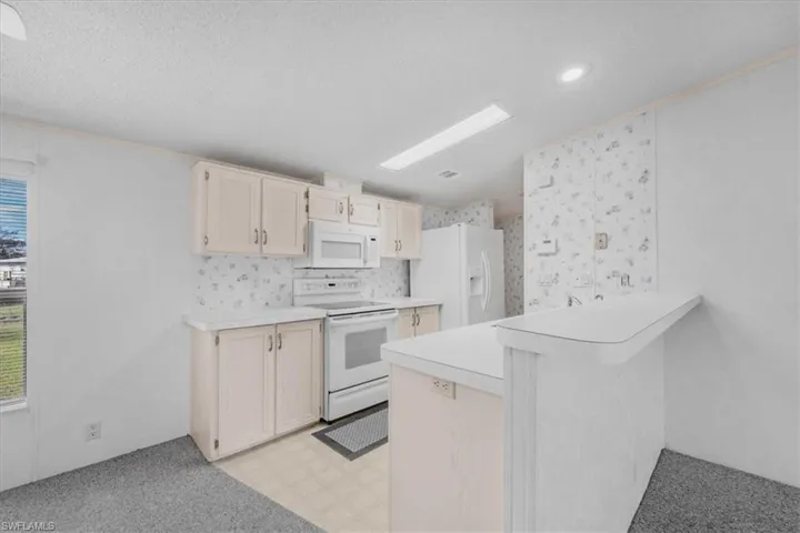 Kitchen with white appliances, light countertops, light floors, a breakfast bar area, and a peninsula