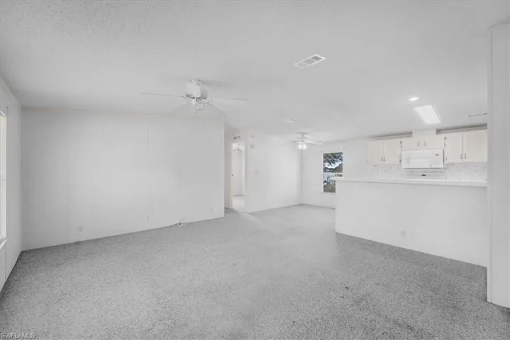 Unfurnished living room with ceiling fan, a textured ceiling, and light colored carpet