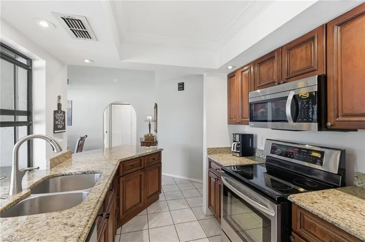 Kitchen featuring appliances with stainless steel finishes, light stone countertops, ornamental molding, recessed lighting, and a tray ceiling