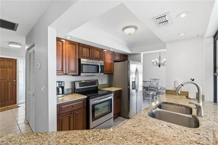 Kitchen with appliances with stainless steel finishes, light tile patterned floors, recessed lighting, light stone countertops, and ornamental molding