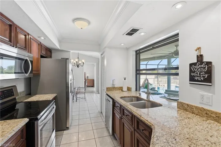 Kitchen with stainless steel appliances, crown molding, a tray ceiling, light stone countertops, and light tile patterned floors