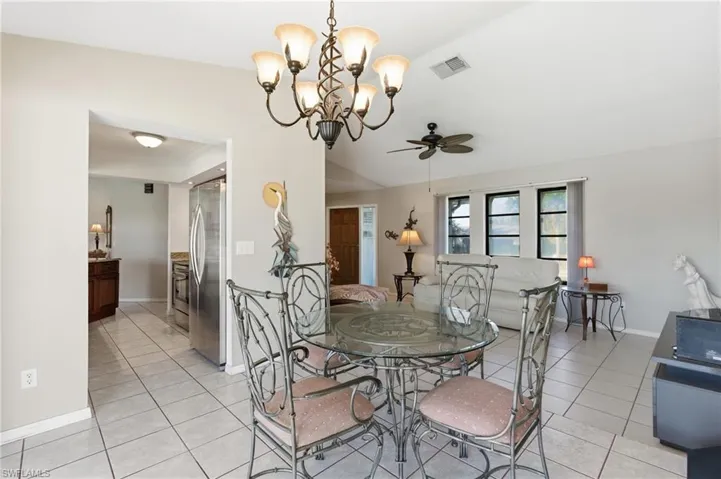 Dining room with ceiling fan, light tile patterned floors, a chandelier, and vaulted ceiling