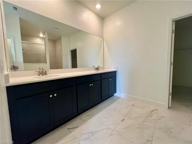 Bathroom featuring light marble finish flooring, double vanity, and tiled shower