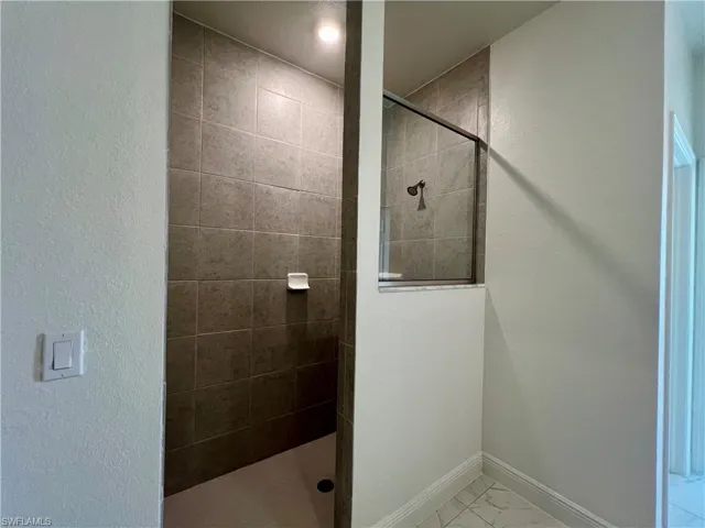 Bathroom with walk in shower, light marble finish floors, and a textured wall