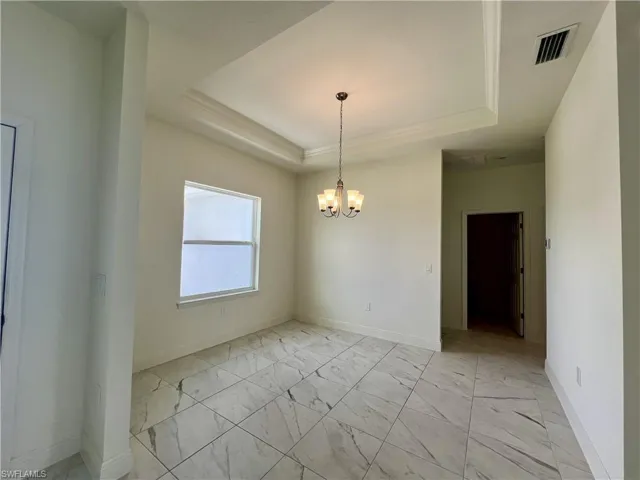 Empty room featuring a raised ceiling, light marble finish flooring, and a chandelier