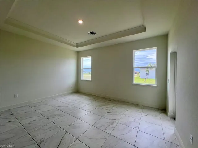 Unfurnished room with a tray ceiling, light marble finish floors, healthy amount of natural light, and crown molding