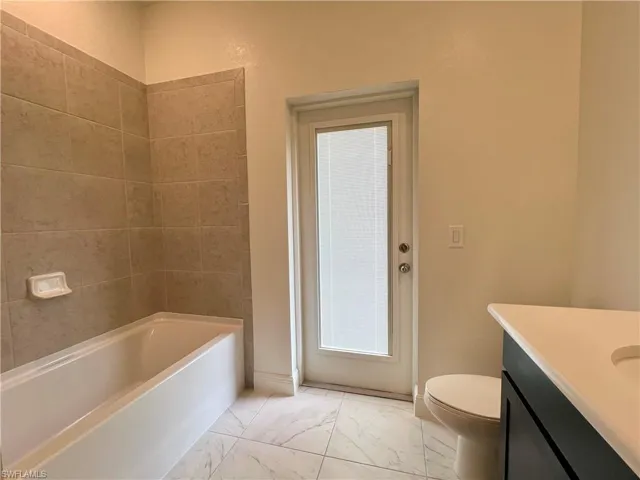 Bathroom with vanity, light marble finish floors, and washtub / shower combination