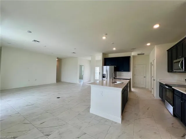 Kitchen featuring dark cabinetry, light marble finish flooring, stainless steel appliances, an island with sink, and recessed lighting