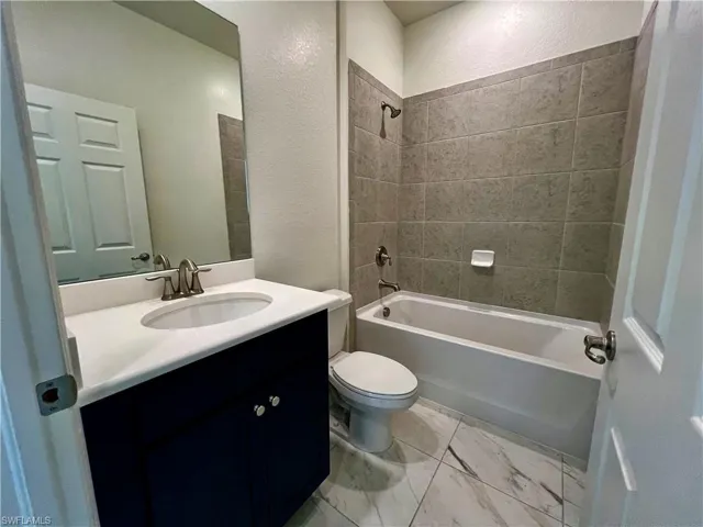 Bathroom featuring tub / shower combination, vanity, a textured wall, and light marble finish floors