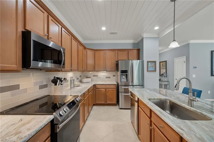 Kitchen with decorative light fixtures, light stone counters, sink, and appliances with stainless steel finishes