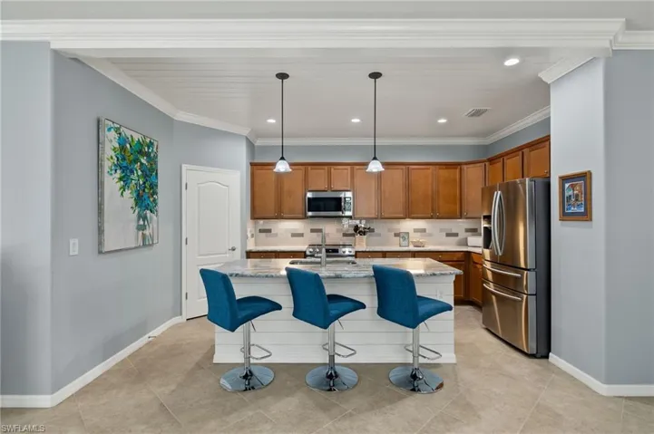 Kitchen featuring stainless steel appliances, tasteful backsplash, decorative light fixtures, a kitchen island with sink, and ornamental molding