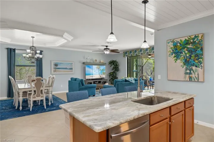 Kitchen featuring sink, hanging light fixtures, light stone counters, a kitchen island with sink, and ceiling fan with notable chandelier