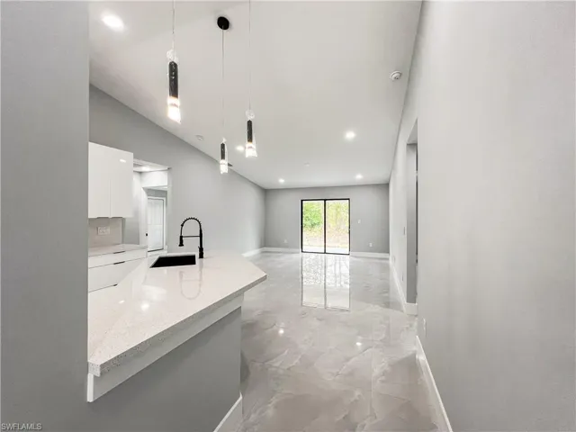 Kitchen with light stone countertops, white cabinets, sink, hanging light fixtures, and vaulted ceiling